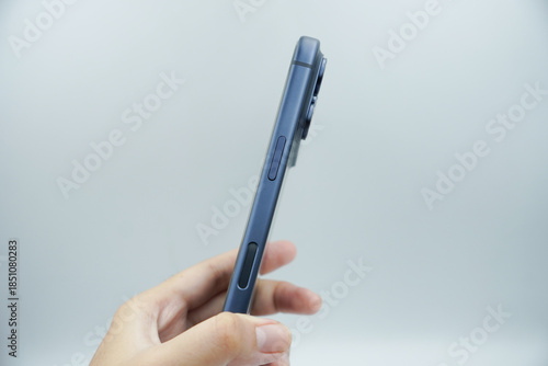 A left hand holds an expensive smartphone in the deep blue variant and shows the volume buttons next to it with a white background.