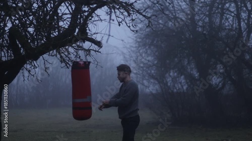 A man in a foggy forest punching a punching bag, a concept of depression and struggle