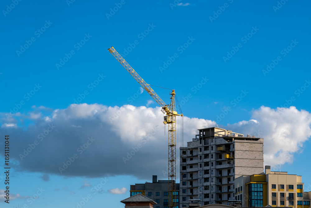 Fototapeta premium Tower Crane and Apartment Building Under Construction Against Cloudy Sky