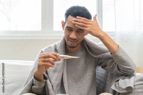 Seasonal cold sickness in people concept, Sick asian man looking at thermometer during measuring his body temperature feel exhausted and headache from fever.