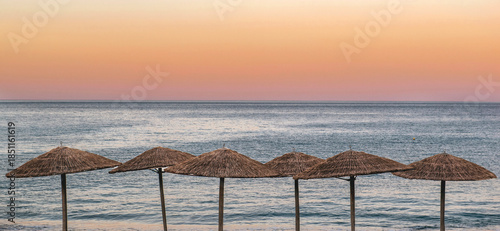 straw umbrella at sunset in front of clear blue sea and colorful sky in Pelop...