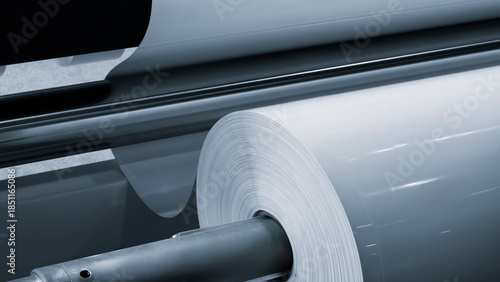 Large industrial automatic machine for cutting and gluing PVC film on wood chipboard and MDF boards for furniture production, rollers with white PVC film are loaded