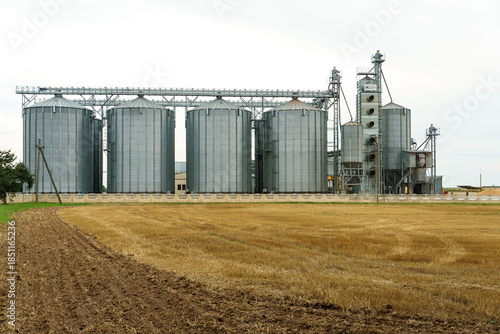 A large modern plant located near a wheat field for the storage and processing of grain crops. view of the granary illuminated by the light of the setting sun against the blue sky. harvest season.