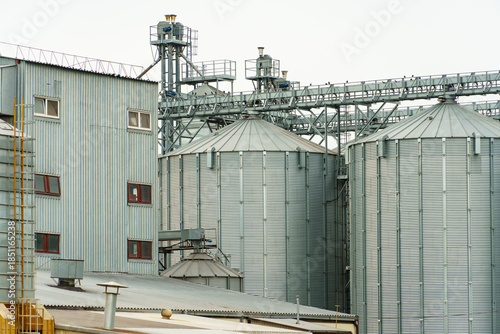 A large modern plant located near a wheat field for the storage and processing of grain crops. view of the granary illuminated by the light of the setting sun against the blue sky. harvest season.