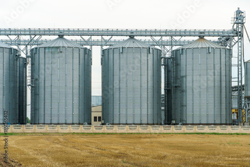 A large modern plant located near a wheat field for the storage and processing of grain crops. view of the granary illuminated by the light of the setting sun against the blue sky. harvest season.