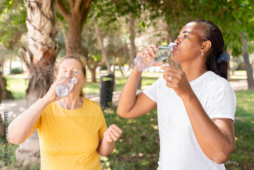 Fotografía Two diverse senior women staying hydrated in a park, drinking bottled water afte