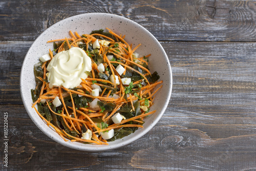 Seaweed and carrot salad with diced egg and dollop of creamy mayonnaise in ceramic bowl