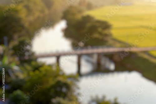 Blur image of Picturesque stone bridge crossing a river surrounded by a beautiful green rice fields and forest during a day