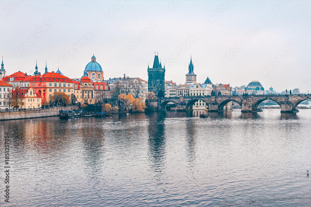 Fototapeta premium Charles Bridge over Vltava River in Prague, Czech Republic. Serene view of medieval stone arch bridge connecting Old Town with Lesser Town, historic architecture and Vltava river under overcast sky