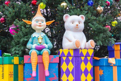 New Year's composition: a polar bear and an elf sit on gift boxes against the backdrop of a decorated Christmas tree.