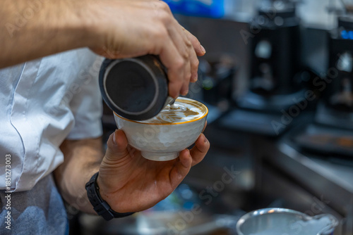 Close-up of a professional barista pouring steamed milk into a ceramic cup to create latte art in a café setting