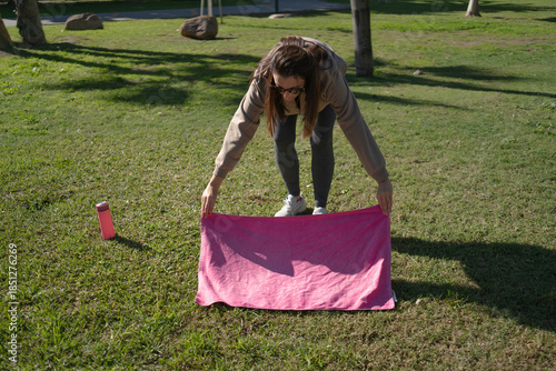 Obraz na plátne Woman spreading pink yoga mat on green grass