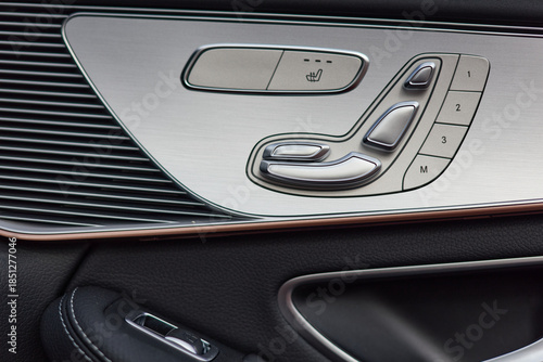 The car interior shows seat adjustment controls on the door panel, including seat heating, memory settings, and adjustable controls. Interior details also feature dark leather.