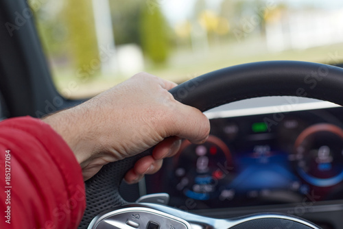 A person is driving a vehicle, with their hand on the steering wheel. The car's dashboard and outside scenery are visible through the windshield.