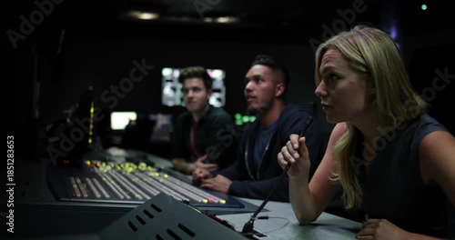 Focused woman operating soundboard with colleagues in a dark studio with cinematic lighting.