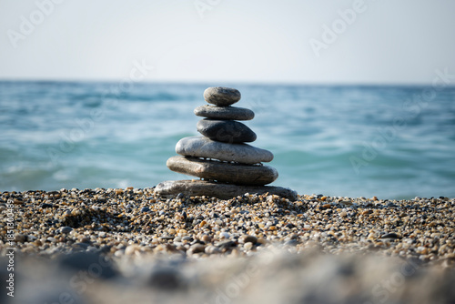 Balanced zen stone tower creating a serene cairn structure on a peaceful pebble beach, with the tranquil blue sea and sky providing a calm background for meditation