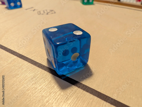Close-up of blue transparent die on wooden board of tabletop game. Gaming, leisure, hobby, dexterity, strategy, skill, entertainment, indoor activity, competition, play, scoring, luck, rolling, pips.