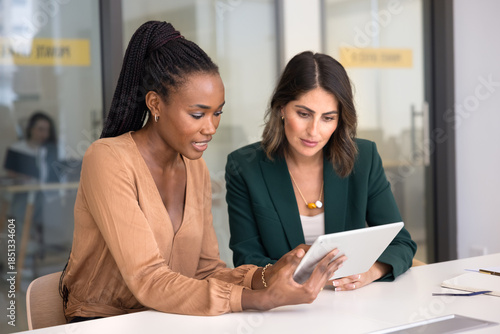Foto Two engaged multiethnic female colleagues using tablet at workplace, reviewing work application