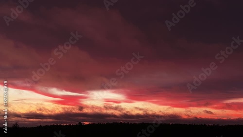 Stunning red and purple clouds moving across the sky during a dramatic winter sunrise, with a dark coniferous forest silhouetted against the colorful horizon in a Scandinavian landscape
