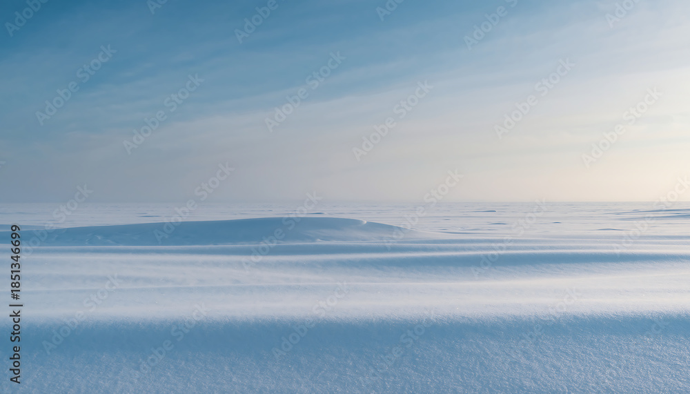 Fototapeta premium A serene landscape of a frozen lake with distant hills under a blue sky with wispy clouds