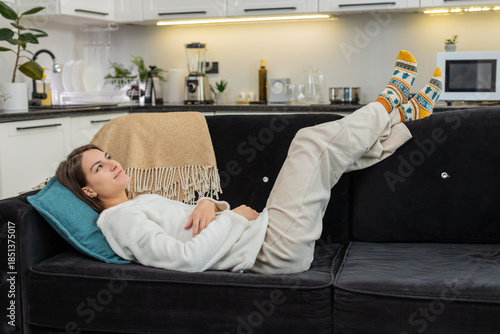 Young woman at home lies back and rests in cool air and calm hush from quiet home tech around. Caucasian girl on sofa lifts feet on back smiles enjoys stable climate control and low noise indoors here