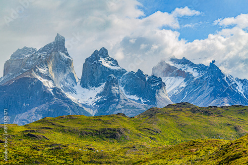 Obraz na plátne Rugged Cuernos del Paine peaks tower over the green hills below as clouds drift across the sky in Torres del Paine National Park, Chile