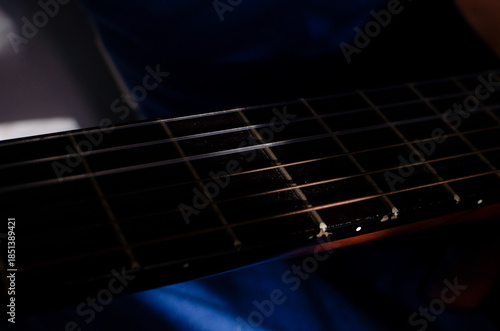 Close-up photo of an acoustic guitar with shadows. Guitar strings, neck, frets and body