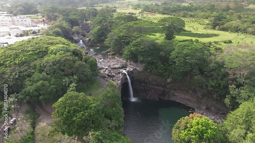 Panoramic Aerial view of Rainbow Falls along Wailuku River waterfall landscape in Hilo Hawaii on the Big Island with lush greenery and water pool - 4K Drone
