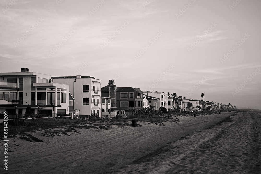 Fototapeta premium Pastel sunset sky above a long row of beachfront homes and sandy shoreline in Sunset Beach, California, capturing calm coastal living at dusk.