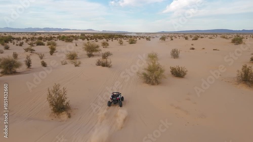 Aerial view of Polaris RZR UTV driving through desert sand dunes at sunset.