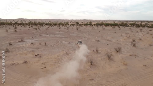 Aerial view of Polaris RZR UTV driving through desert sand dunes at sunset.