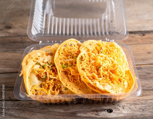 Savory crepe-like snacks with a shredded topping in a clear plastic container atop a rustic wooden surface