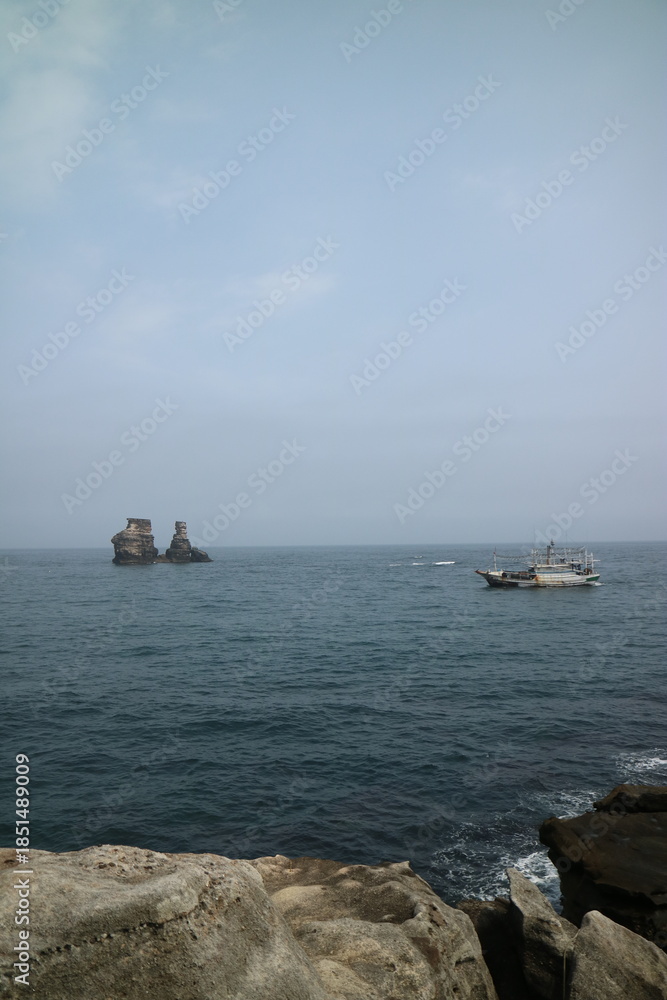 Obraz premium Fishing Boat Sailing Near Coastal Rock Formations