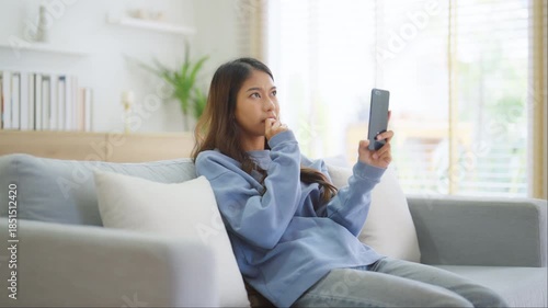 Happy young asian woman relaxing at home. Female smiling and talking chat with friend sitting on sofa and holding mobile smartphone. Girl using video call to close friend