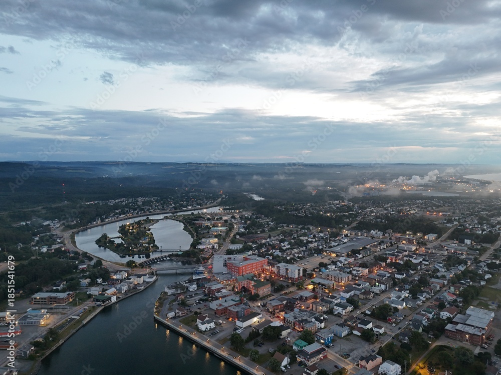 Fototapeta premium Aerial view of Matane city at dusk with river, fog, low clouds and city lights along St Lawrence River, Quebec, Canada. g.