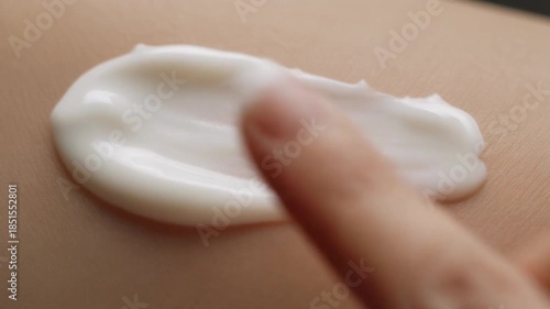 Finger applying white cream to skin for moisturizing