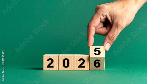 Wooden blocks symbolizing the transition from 2025 to 2026, with a hand placing the final block