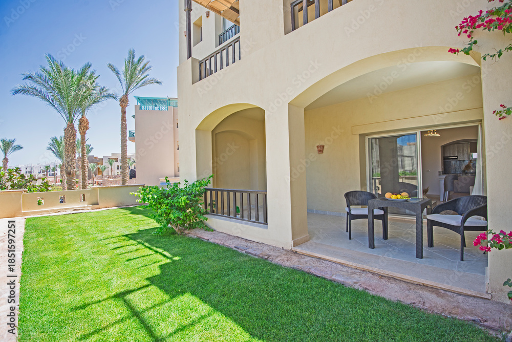 Naklejka premium Terrace furniture of a luxury apartment in tropical resort with furniture and sea view over garden from balcony