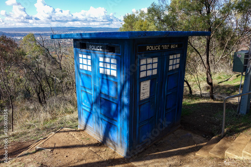 Obraz na plátně A Whimsical Blue Police Public Call Box Replica Stands on a Sunny Hill Overlooki