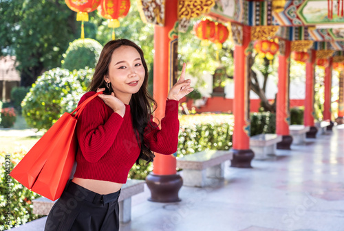 Portrait of joyful young asian woman celebrates Chinese New Year at chinese temple, showcasing her bright red shopping bags against a stunning shrine backdrop. A moment of happiness