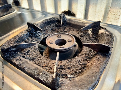 Side view of dirty gas stove burner with thick carbon buildup and grease