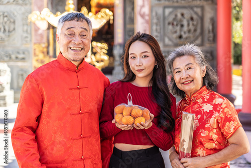 During the Lunar New Year at a beautiful Chinese temple, a cheerful teenage daughter presents her parents with oranges, symbolizing love and respect. Together, they cherish this festive tradition.