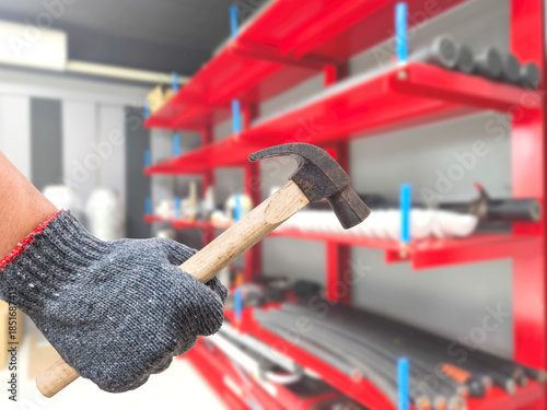 Worker hand holding rustic hammer over working rooom or warehouse background in factory..
