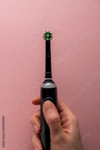 Electric toothbrush in female hand on pink background
