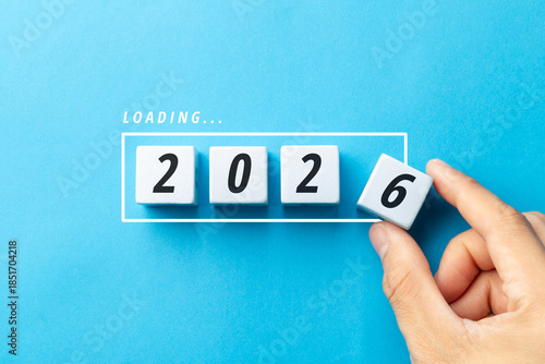 Hand completing the year 2026 by placing the final white number block on a blue background. Minimalist concept of achievement, goal setting, and strategic preparation for the future.