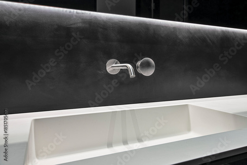 Stainless steel faucet on a black wall in a minimalist bathroom interior
