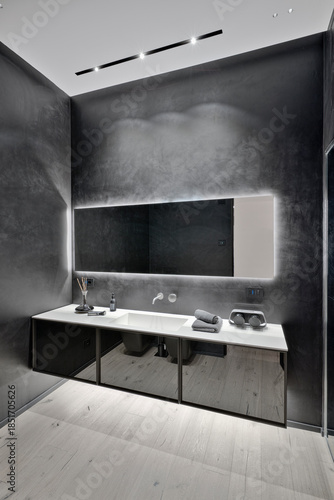 Modern black bathroom interior with parquet flooring and sink cabinet in the foreground.