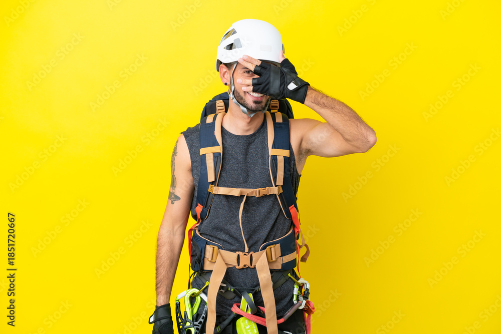 Fototapeta premium Young caucasian rock climber man isolated on yellow background covering eyes by hands and smiling