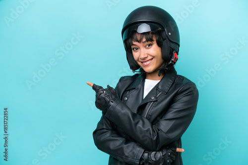 Young Argentinian woman with a motorcycle helmet isolated on blue background pointing finger to the side
