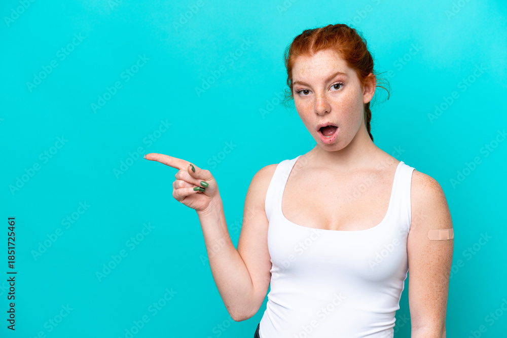 Fototapeta premium Young reddish woman wearing a band aids on blue background surprised and pointing side